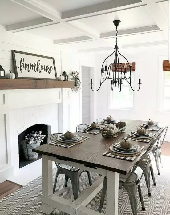 a simple modern farmhouse dining area with a white fireplace, signs and pumpkins, a wooden table and metal chairs