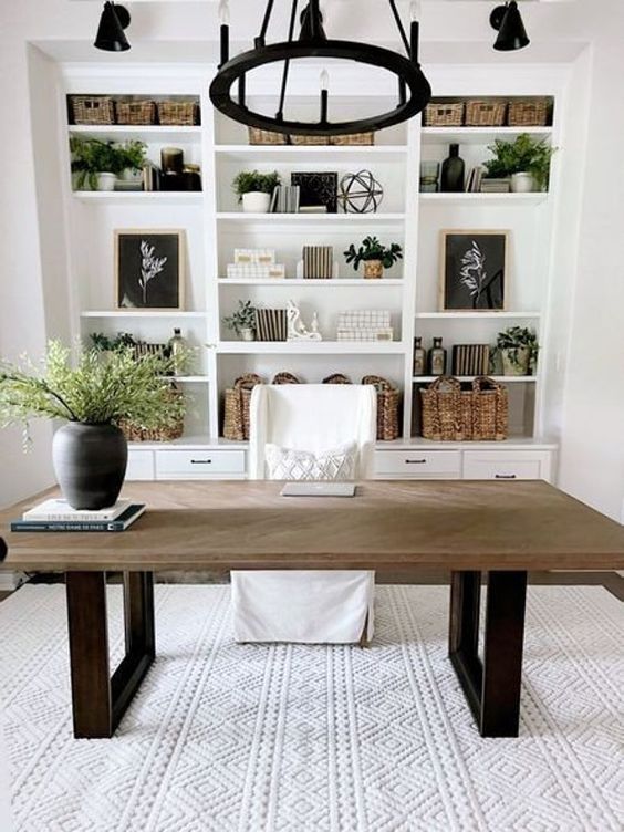 a simple modern farmhouse home office with a large white built-in storage unit, a heavy desk, a white chair, a black chandelier