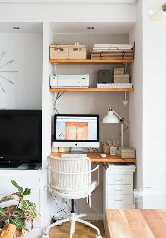 a small and chic home office nook in the living room, with wall-mounted shelves and a desk, a file cabinet, a PC and a lamp