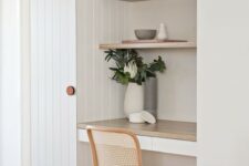 a small and clean working nook with a couple of built-in shelves and a desk, a woven chair, potted greenery and decor