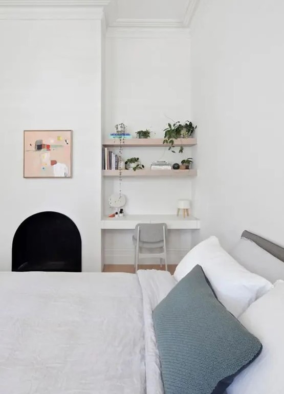 A small awkward nook done with built in shelves and a desk, a grey chair, potted greenery and books is a lovely space