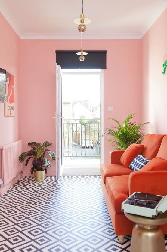 a small bright living room with pink walls, an orange sofa, a gallery wall and potted plants for more glam
