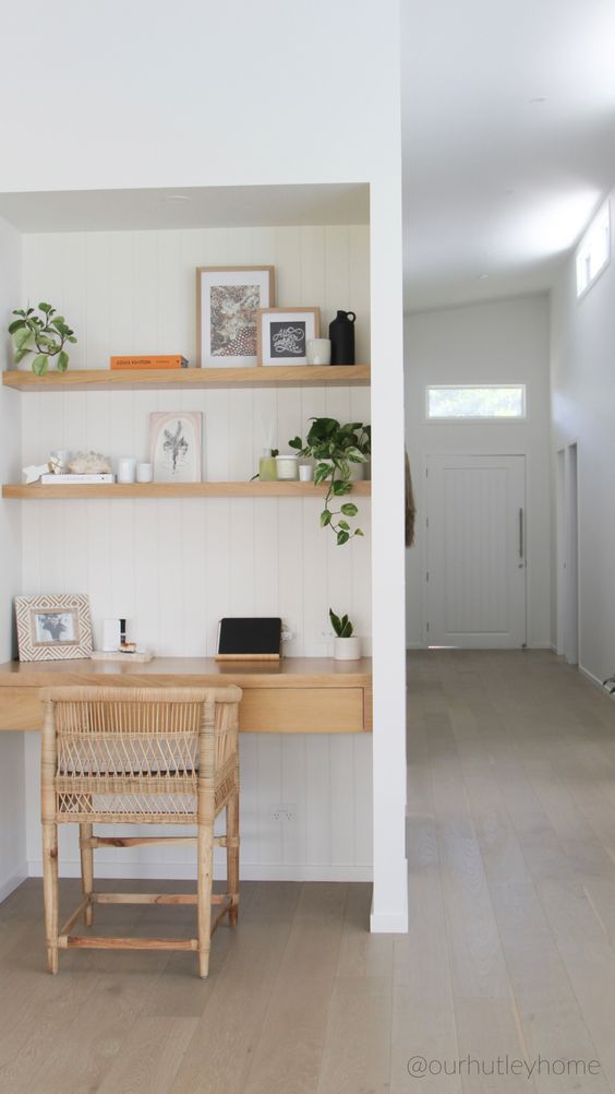 A small niche with white shiplap, built in shelves and a desk with drawers, a rattan chair, some greenery and lovely decor