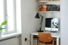 a small nook by the window with a white desk and some suspended shelves, a plywood chair and a black table lamp