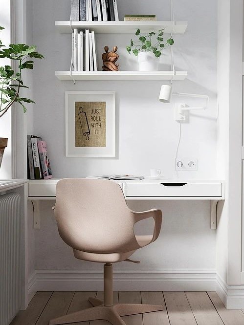 a small yet cool home office nook in the living room created with IKEA items - shelves, a desk and a blush chair plus a white sconce