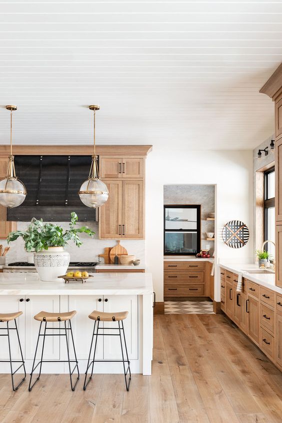 a stained modern farmhouse kitchen with a white kitchen island, tall wooden stools and pendant lamps is cozy