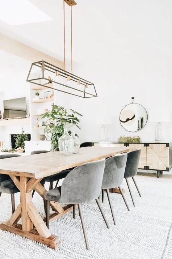 a stylish modern country dining room with a trestle table, grey chairs, a metal chandelier, an inlaid console and a round mirror