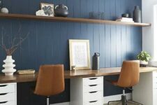 a stylish modern country home office with a navy planked accent wall, a shared desk, leather chairs, a long floating shelf for storage
