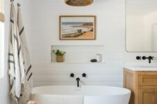 a stylish modern farmhouse bathroom done in neutrals, with shiplap on the walls, white hex tiles, a timber vanity, a mirror, a woven pendant lamp and an oval tub