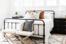 a stylish modern farmhouse bedroom with a row of windows, a wrought bed with neutral bedding, stools and black nightstands