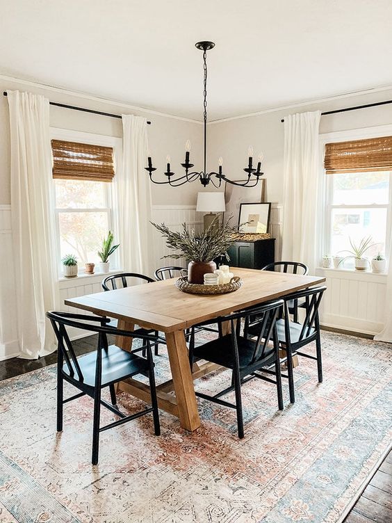 a stylish modern farmhouse dining space with a stained table, black chairs and a black cabinet, layered curtains and a printed boho rug
