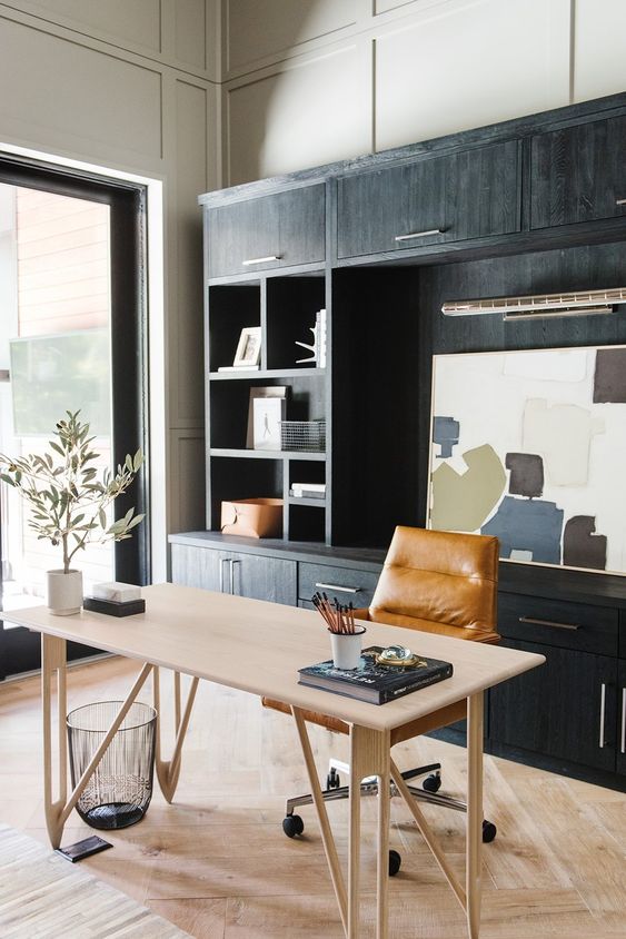 a stylish modern farmhouse home office with a black storage unit, a lightweight desk, an amber leather chair and some art