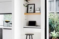 a super tiny working nook with built-in shelves and a small desk with drawers, a black stool, artworks and a potted plant