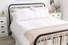a sweet farmhouse bedroom with a forged bed, white nightstands, pink blooms and a sweet pink blanket