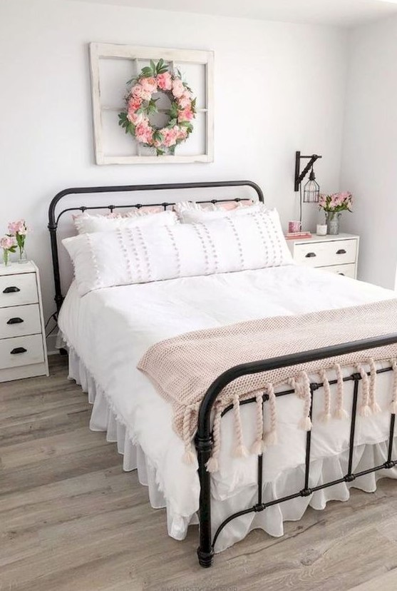 a sweet farmhouse bedroom with a forged bed, white nightstands, pink blooms and a sweet pink blanket