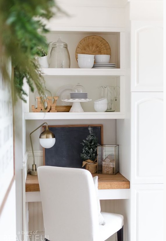 a tiny home office space in the kitchen, with just a small built-in desk, a white chair and a brass lamp plus a chalkboard