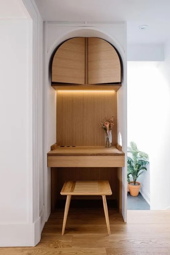 a tiny nook turned into a working space clad with plywood, with a storage unit and a built-in desk, a stool and built-in lights