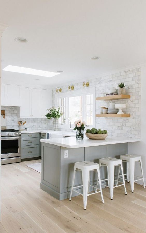 A two tone modern farmhouse kitchen with white and grey cabinets, open shelves, white marble tiles and metal stools