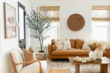a warm modern farmhouse living room with an amber leather sofa, neutral chairs, a pouf, a coffee table and some decor