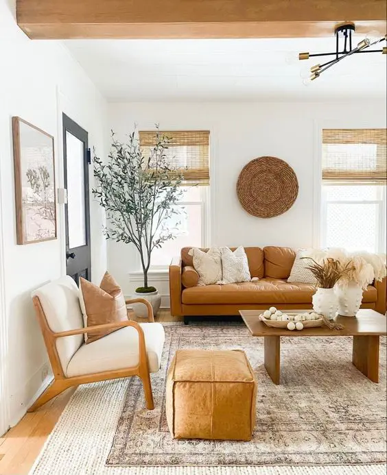 a warm modern farmhouse living room with an amber leather sofa, neutral chairs, a pouf, a coffee table and some decor