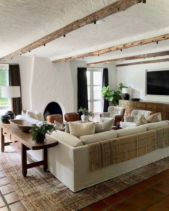 a welcoming Spanish farmhouse living room with a fireplace, a stained sideboard, a neutral sofa, a console table, cozy chairs