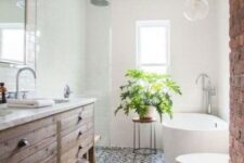 a welcoming farmhouse bathroom with a stained vanity, a brick wall, a mosaic tile floor and an oval tub