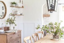 a welcoming farmhouse dining room with a light-stained table and chairs, wicker chairs, a stained credenza, metal lanterns and greenery
