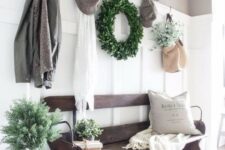a welcoming farmhouse entryway with a weathered wooden bench, a wire basket, a sign, some decor and a boxwood wreath