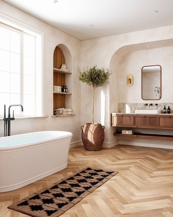 a welcoming modern farmhouse bathroom with a niche and a floating vanity, an arched niche with shelves, an oval tub, a boho rug and a potted tree