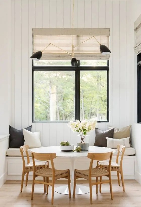 A welcoming modern farmhouse dining space with a built in bench, a round table, woven chairs, touches of black and woven shades