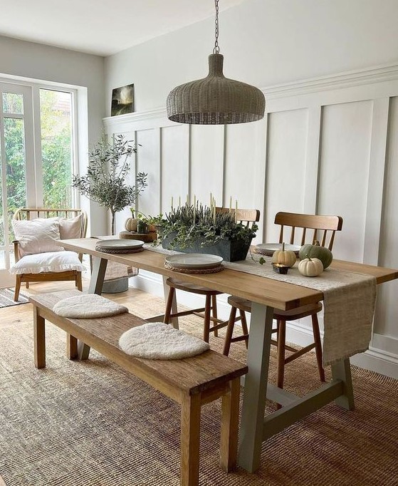 a welcoming neutral dining space with a stained trestle table, bench and chairs, a woven pendant lamp and potted plants