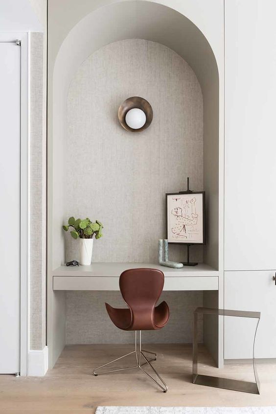 An ached niche with a built in desk, some art, a sconce and a burgundy chair is adorable and chic