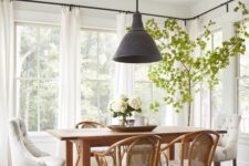 an airy dining room with a stained table and rattan chairs, a black pendant lamp, a potted tree and a neutral rug
