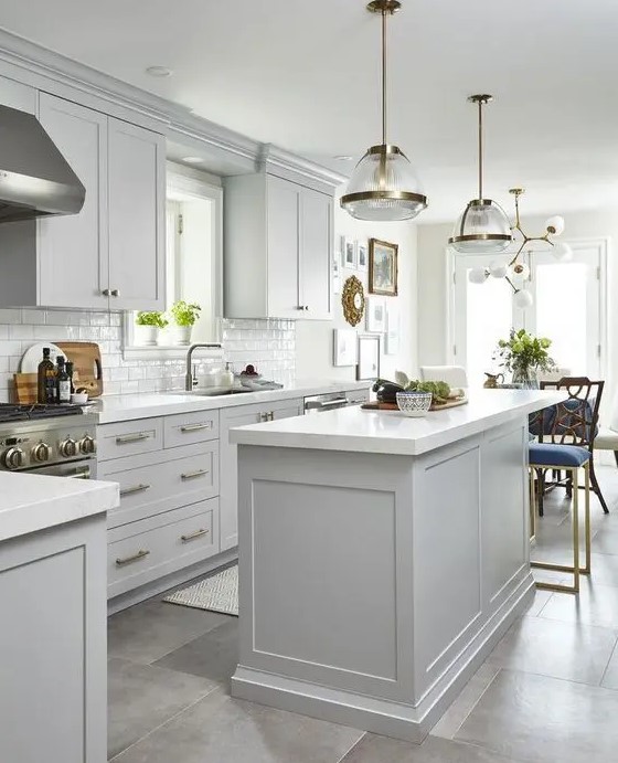 an airy dove grey kitchen with shaker cabinets, a white subway tile backsplash and white countertops and chic pendant lamps