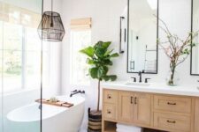 an airy modern farmhouse bathroom with a double timber vanity, framed mirrors, an oval tub, a boho rug, a black pendant lamp and a boho rug