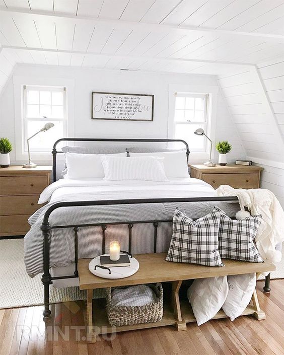 an airy modern farmhouse bedroom with a wrought bed with neutral bedding, a stained bench with pillows, matching nightstands and potted greenery