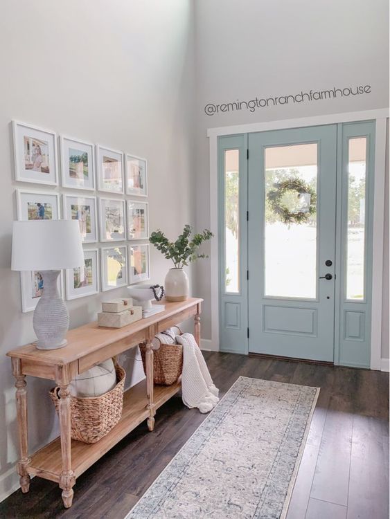 an airy modern farmhouse entry with a console, a grid gallery wall, baskets and pillows, a blue door and a rug