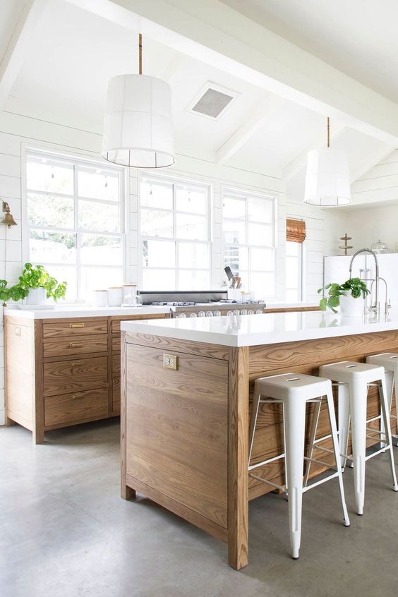 an airy modern farmhouse kitchen with stained cabinets and a kitchen island, white stone countertops, pendant lamps