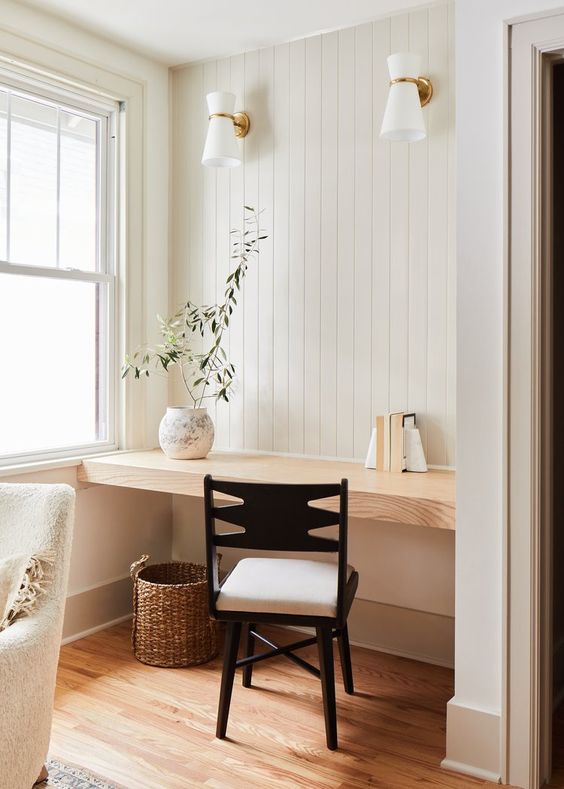An airy modern farmhouse nook by the window, with a built in desk, a neutral chair, some sconces and a basket