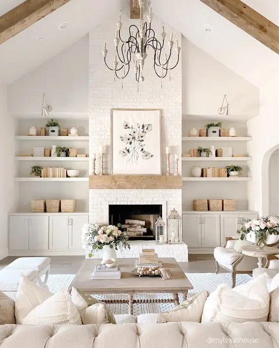 An all white modern farmhouse living room with built in shelves and cabinets, a fireplace, a chandelier, a coffee table and a sectional