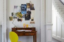 an arched niche with a tiny vintage desk, a yellow chair, an inspirational board with photos and a table lamp