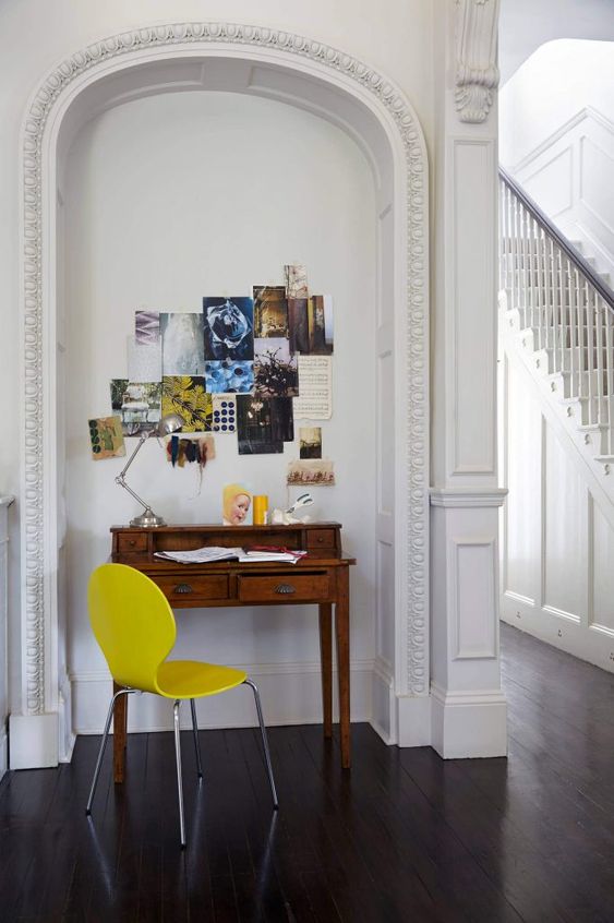 an arched niche with a tiny vintage desk, a yellow chair, an inspirational board with photos and a table lamp