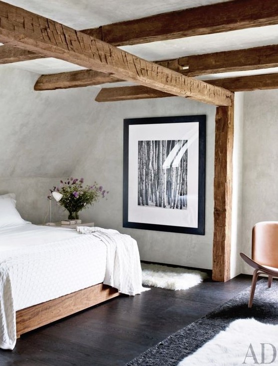 an attic bedroom with a stained bed, stained wooden beams, a leather chair and neutral bedding is a cool idea