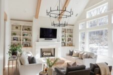an attic modern farmhouse living room with built-in shelves and cabinets, white sofas, grey chairs, a couple of heavy chandeliers