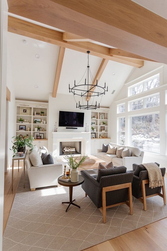 An attic modern farmhouse living room with built in shelves and cabinets, white sofas, grey chairs, a couple of heavy chandeliers