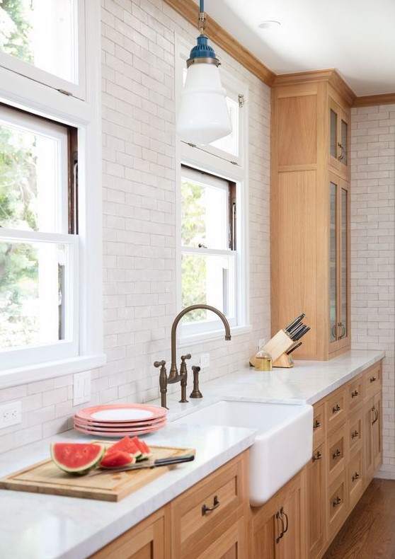 An elegant kitchen with light stained shaker style cabinets, a white subway tile backsplash, white stone countertops