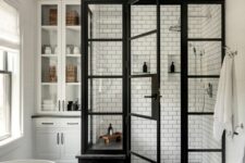 an elegant modern farmhouse bathroom with a shower space done with white subway tiles, a black tub, large scale tiles and a built-in storage unit