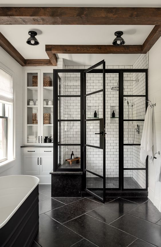an elegant modern farmhouse bathroom with a shower space done with white subway tiles, a black tub, large scale tiles and a built-in storage unit