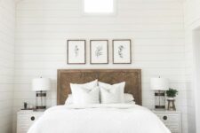 an elegant modern farmhouse bedroom with a bed with a wooden headboard, a stained bench and white nightstands, a gallery wall