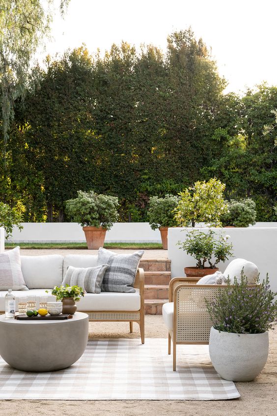 an elegant modern farmhouse terrace with cane seating furniture, potted greenery and blooms and a concrete side table